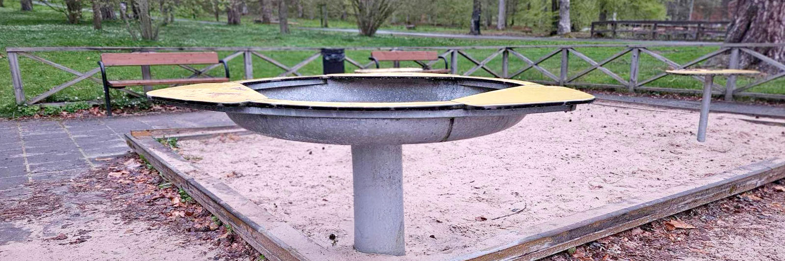 Un grand bac à eau en forme de fleur placé dans un coin d'un bac à sable permet aux enfants de jouer avec l'eau et le sable dans une aire de jeux.